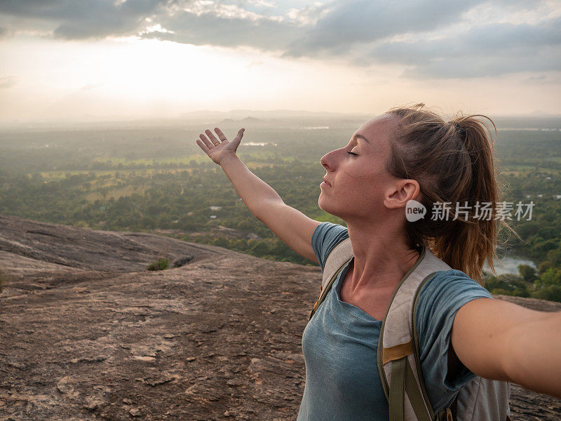 年轻女子在岩石上张开双臂拥抱夕阳