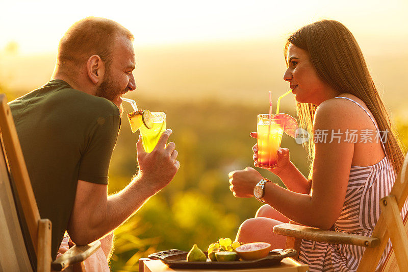 年轻的夫妇在甲板上享受夏日，鸡尾酒和充气