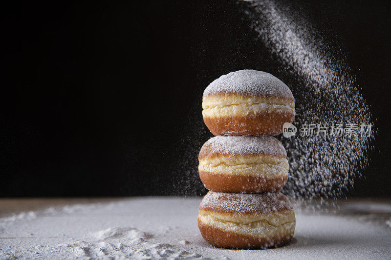 在黑色背景上撒上糖粉的欧洲甜甜圈。