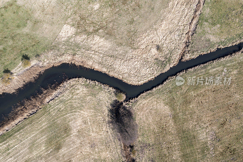 这是无人机拍摄的一张照片，从上面可以看到田野和灌木丛之间的一条小河和一条沙沟。