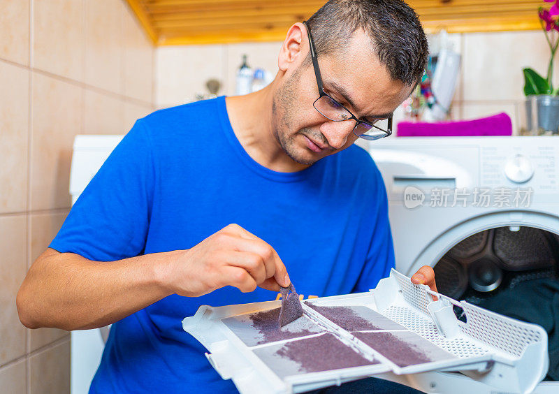 年轻人正在清理滚筒式干燥机的灰尘过滤器上的棉绒。衣物烘干机过滤器里的灰尘和污垢。洗衣过程