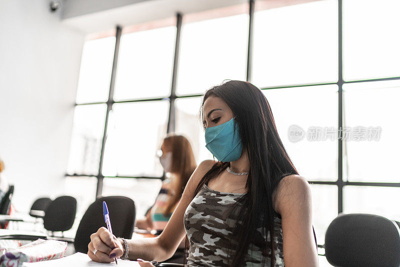 女学生在大学里做笔记或考试——戴着口罩