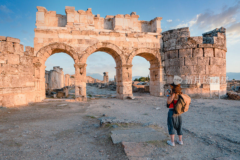 在棉花堡希拉波利斯的古遗迹中，一名女游客正在为Frontinus门拍照