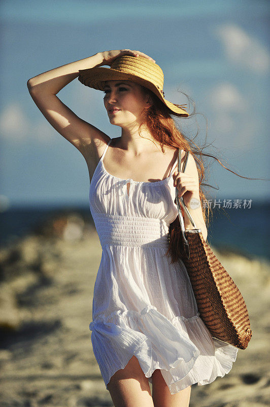 穿着白色背心裙和帽子的年轻女子在海滩上