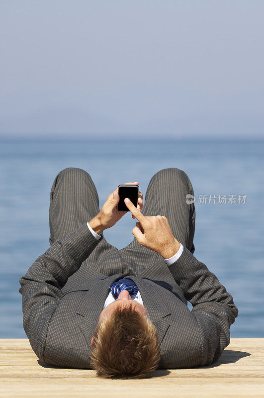 拥有智能手机的商人躺在阳光码头上