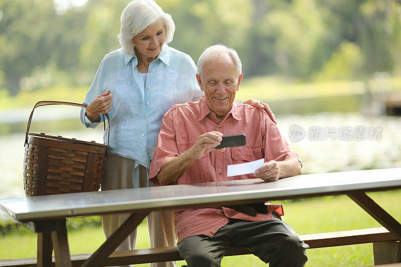 快乐的老年夫妇用智能手机存款支票