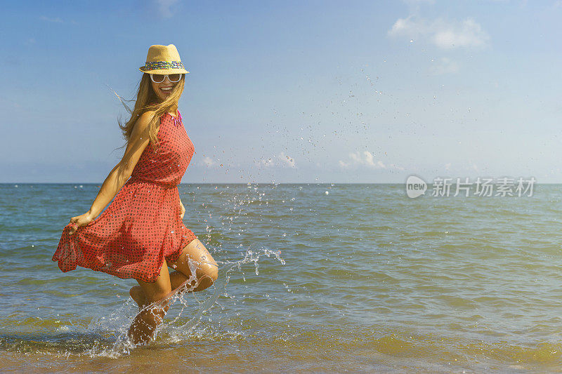 快乐的女孩穿着红色的裙子在沙滩上蹦蹦跳跳