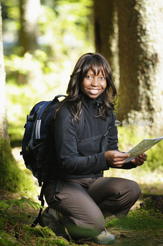 非洲裔美国女性背着一个背包，拿着地图和微笑