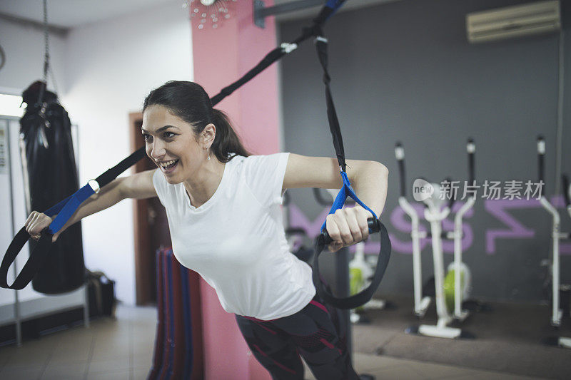 女人在健身房训练与trx健身条手臂