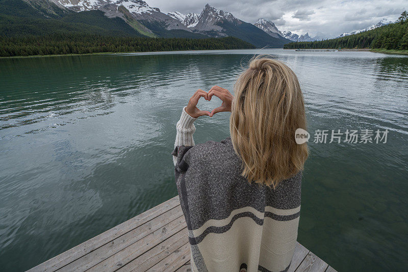 年轻女子在山湖上做心形手指架