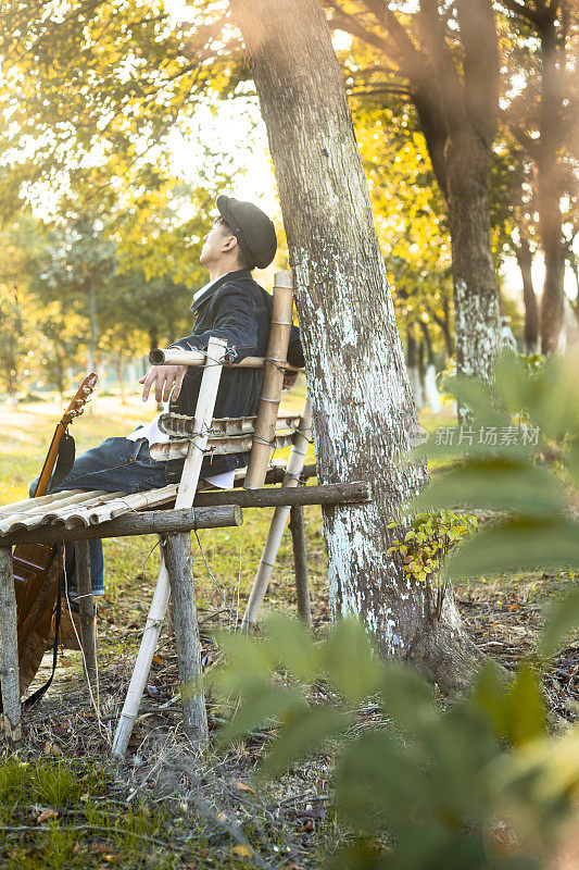沉思的年轻人坐在木凳上，手里拿着吉他