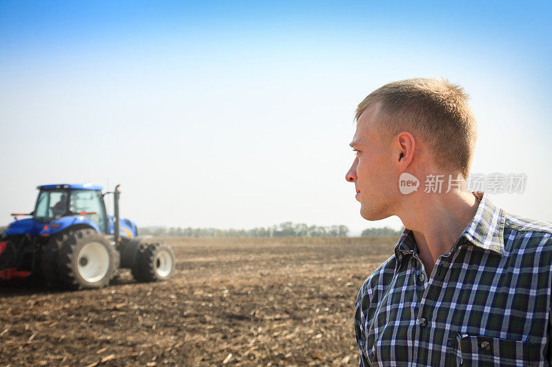 一个年轻人在田里，背景是一台拖拉机。