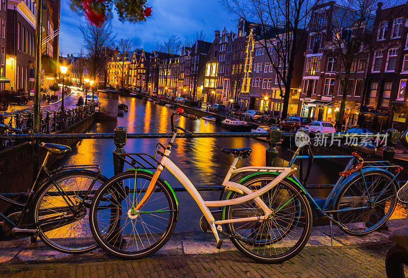 阿姆斯特丹运河和桥的夜间照明，有典型的荷兰房屋，船只和自行车。