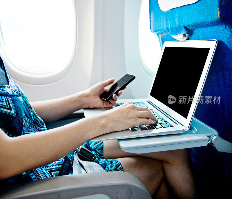 女性在飞机上使用智能手机和笔记本电脑