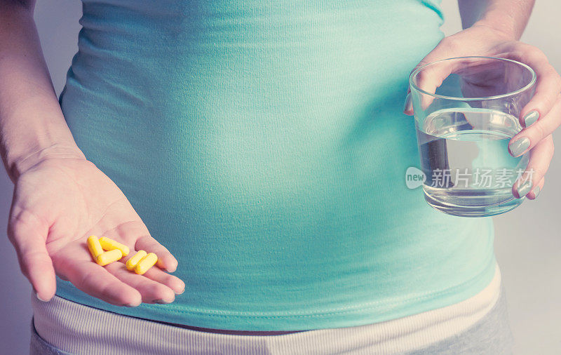一名怀孕三个月的妇女穿着一件蓝色的t恤，里面装着几粒胶囊，另一粒里装着一杯水。体外受精。