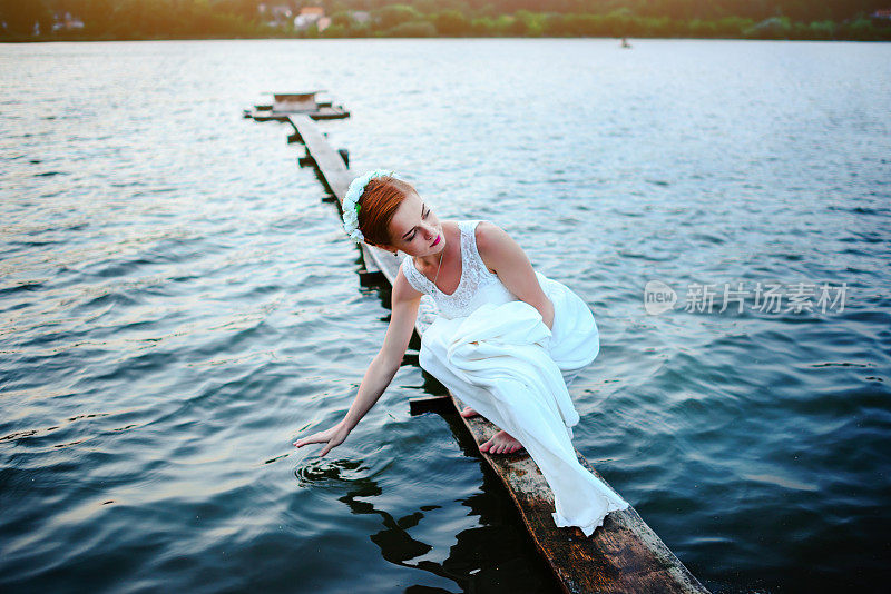 新娘站在码头靠近水，穿着白色的裙子