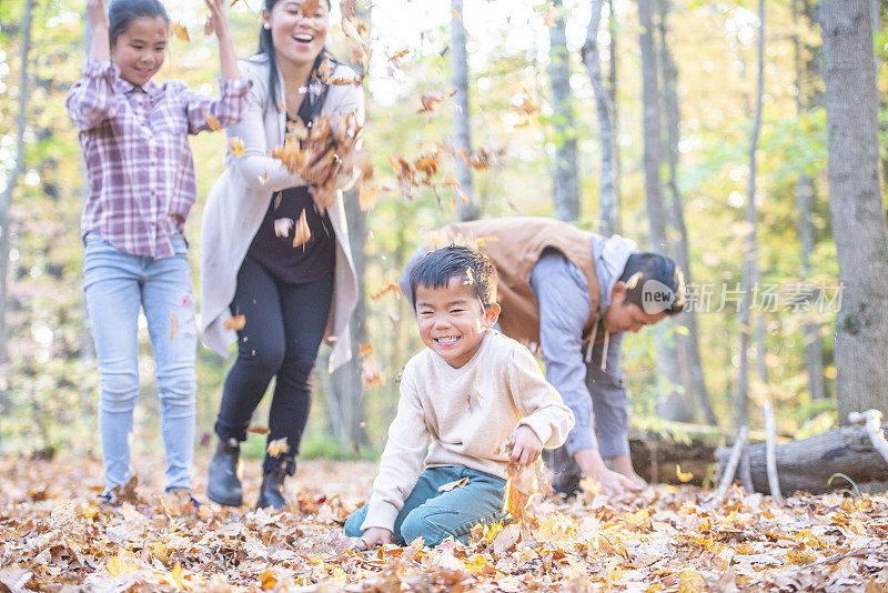 小男孩和家人在树叶间玩耍，看着镜头