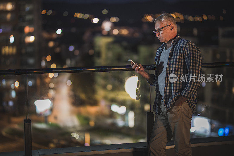 一个老人晚上在顶层公寓的露台上用手机。