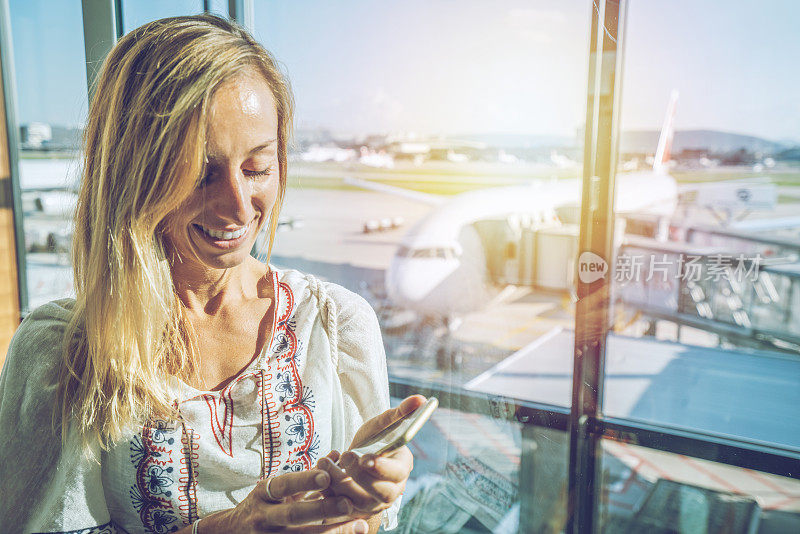 年轻女子在机场等待航班时用智能手机发短信