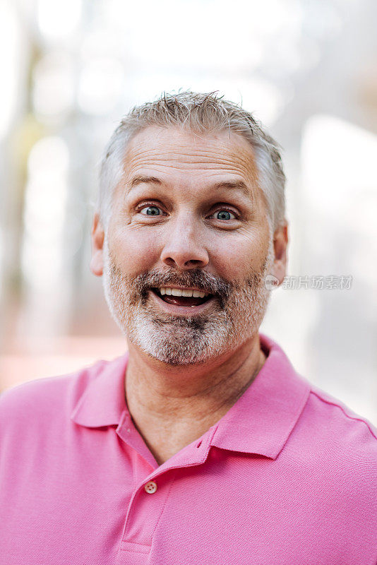 成年白人男子的肖像与灰色头发在粉红色polo衫与惊讶的面部表情