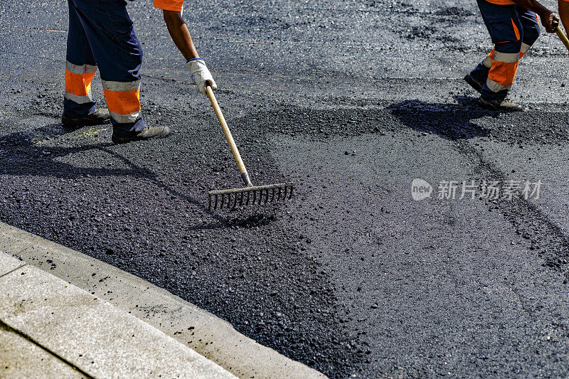 工人们用耙子在路上铺沥青