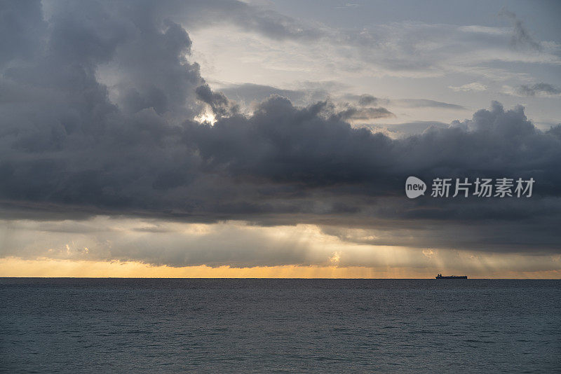 在冬季斯里兰卡的Hikkaduwa，印度洋上壮观的天空下，巨大的雨云下，地平线上的货船。