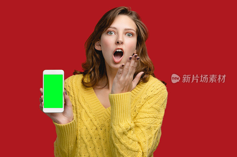 手机复制空间模板。摄影棚里的女人拿着红色背景的智能手机。概念与人空白屏的小玩意。使用广告及应用设备者