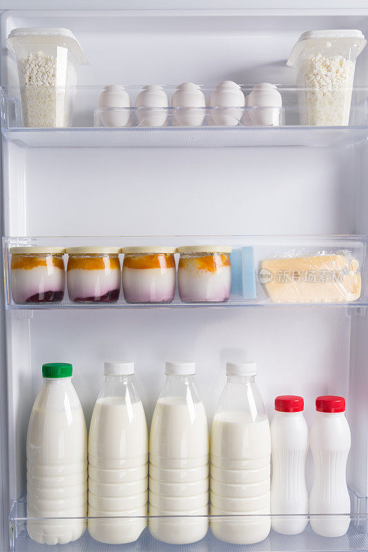 在白色冰箱的门上，架子上放着瓶装的鸡蛋、奶酪、酸奶、白软干酪和牛奶