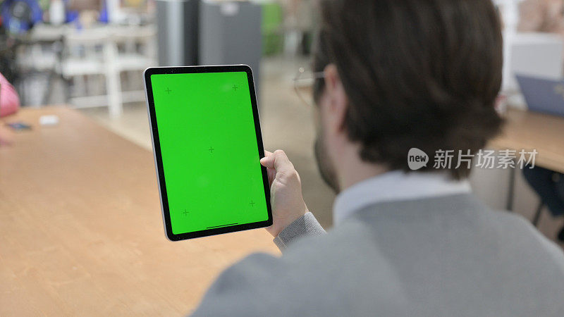 一名男子在看带有绿色色度屏幕的平板电脑
