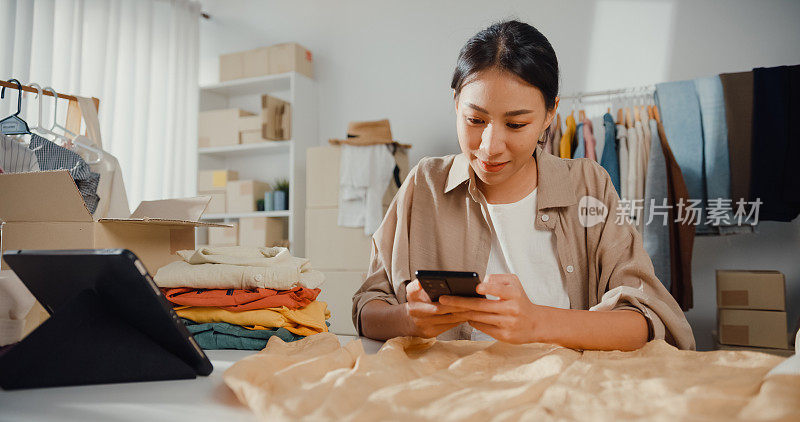 年轻的亚洲小企业主女性在家里使用智能手机检查订单。