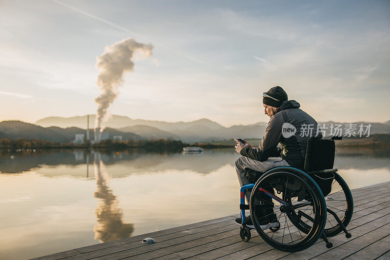 日落时分，在湖边的码头上，坐轮椅的截瘫者使用手机