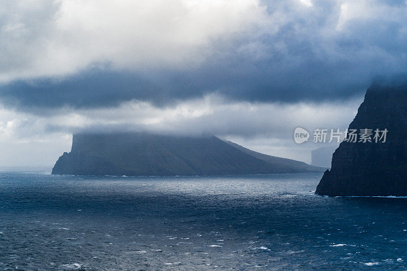 法罗群岛的海景从渡轮在波浪的水域。暴风雨天气，有很大的云景和一些阳光。