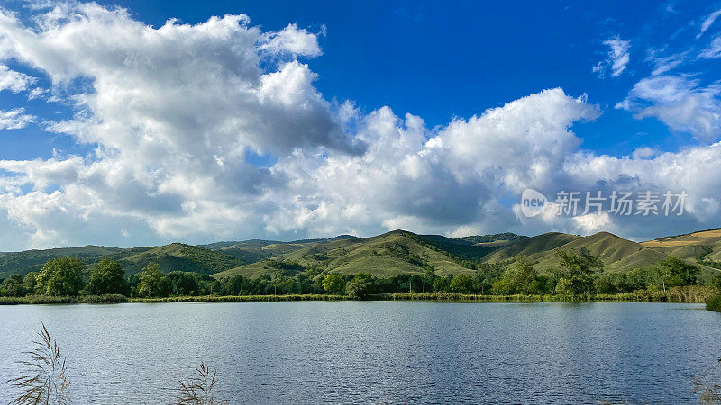 完美的风景:一条河流靠近绿色的山脉，上面是一片云雾密布的天空