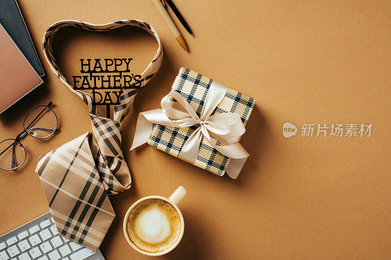 父亲节快乐贺卡模板。将领带、礼品盒、咖啡杯、键盘、纸质笔记本平铺在棕色桌面上。