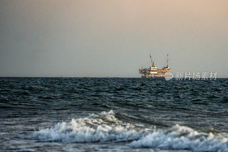 大型天然气和石油海上钻井平台在平静的海面上，在一个晴朗的傍晚，远处的背景是卡特琳娜岛