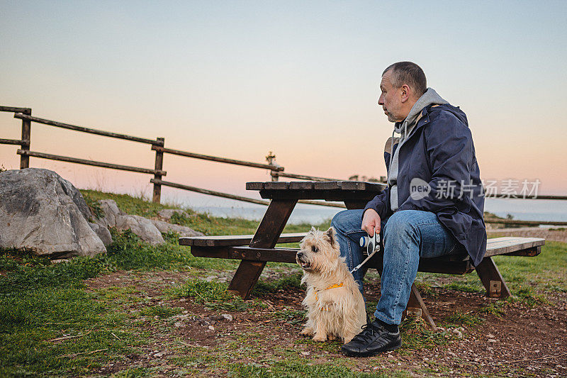 成熟的男人在日落时和狗一起享受大海