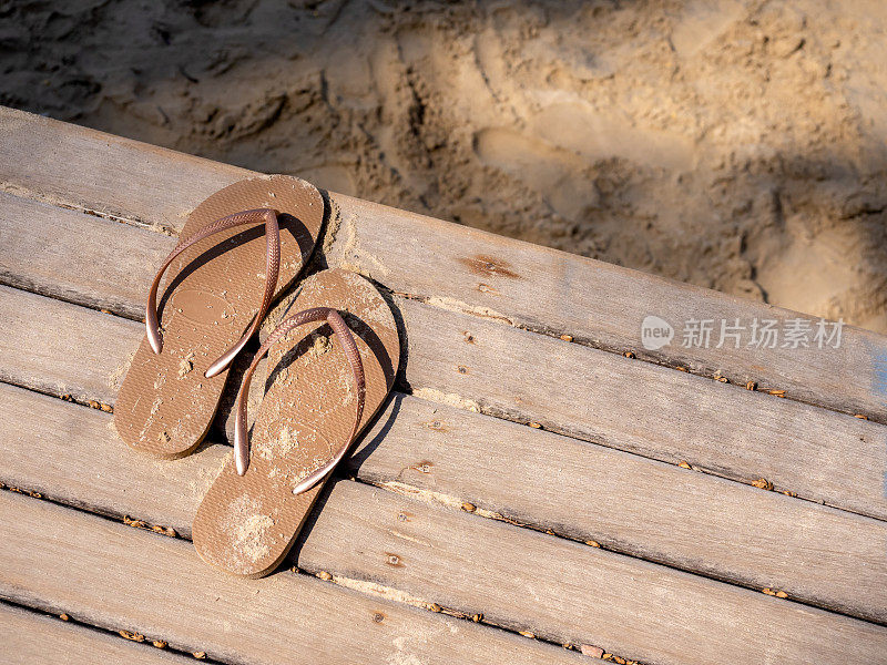 空沙沾污的女子凉鞋被脱下，在木甲板的露台上，走到沙滩上散步，夕阳下，有copy的空间。暑假、假日周末到海边旅游的概念。