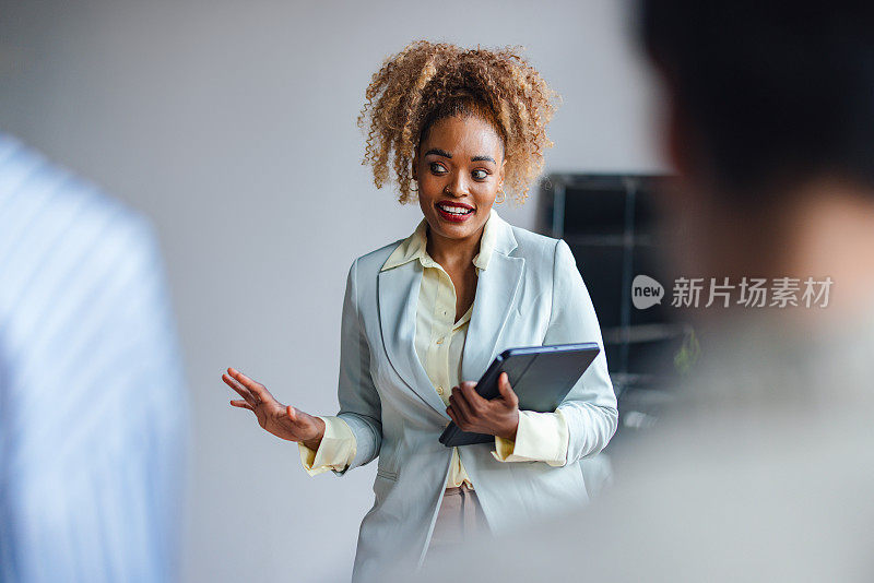 微笑自信的非裔美国女主持人站在她的同事面前，拿着平板电脑与他们互动