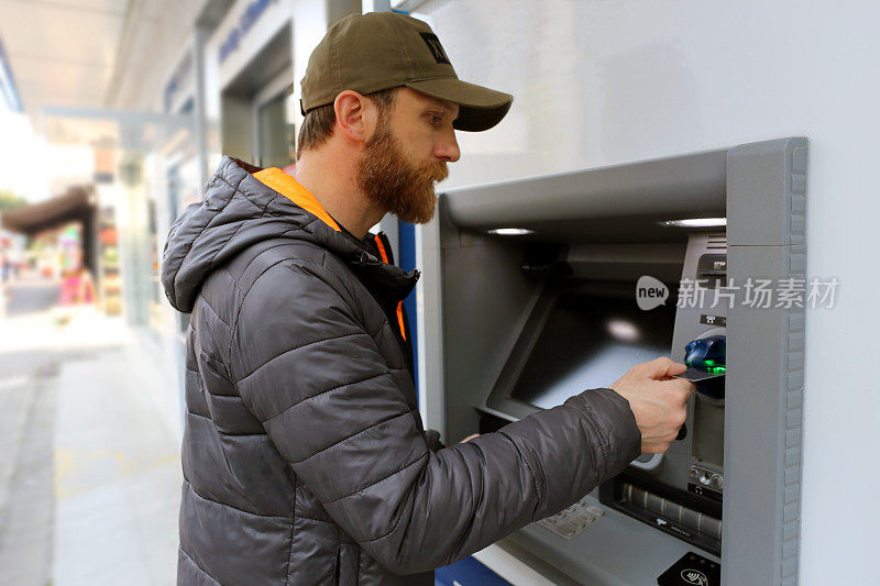 一位留着胡子、戴着帽子的银行顾客，使用借记卡和信用卡通过自动柜员机完成交易