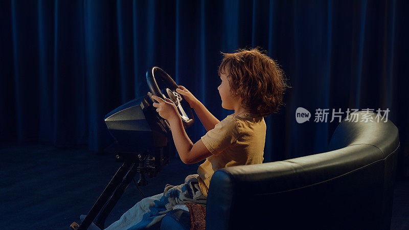卷发男孩在玩电脑游戏，驾驶着游戏方向盘