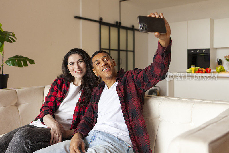 年轻的多种族夫妇在家里舒适的沙发上用智能手机自拍
