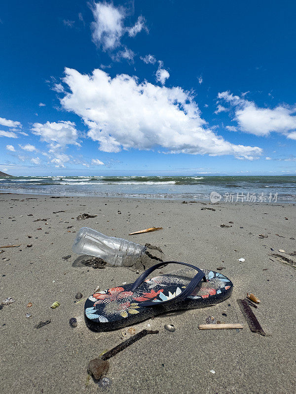 沙滩上，一只废弃的人字拖鞋躺在空塑料水瓶旁边