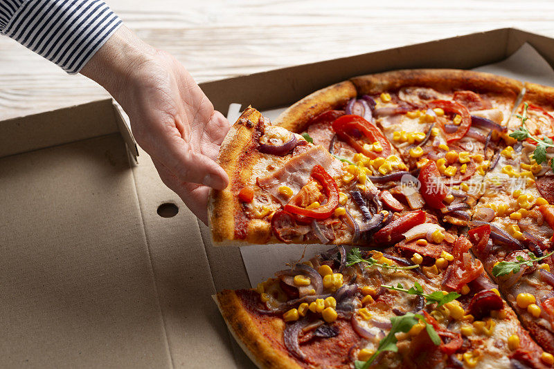 白种人的手从白色木桌上的纸盒里取出一片大披萨