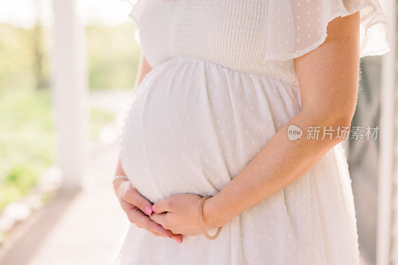 一名孕妇穿着白色连衣裙，抱着她逐渐隆起的腹部。