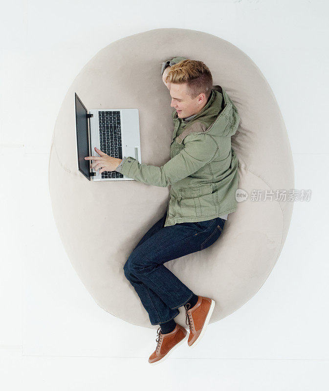 白种年轻男性躺在白色背景下，穿着运动夹克，使用笔记本电脑