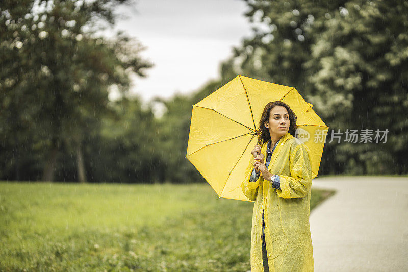 女人穿着雨衣，撑着雨伞，在雨天行走