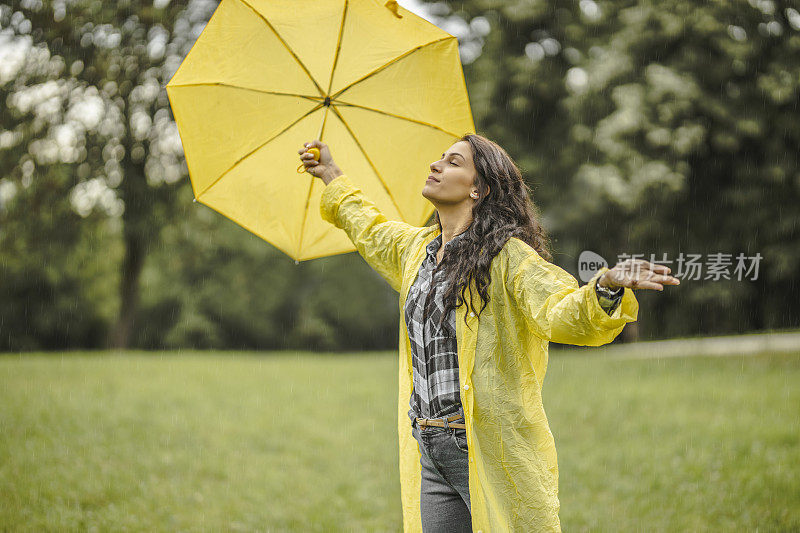 拿着黄伞，穿着黄雨衣，享受着雨的女人