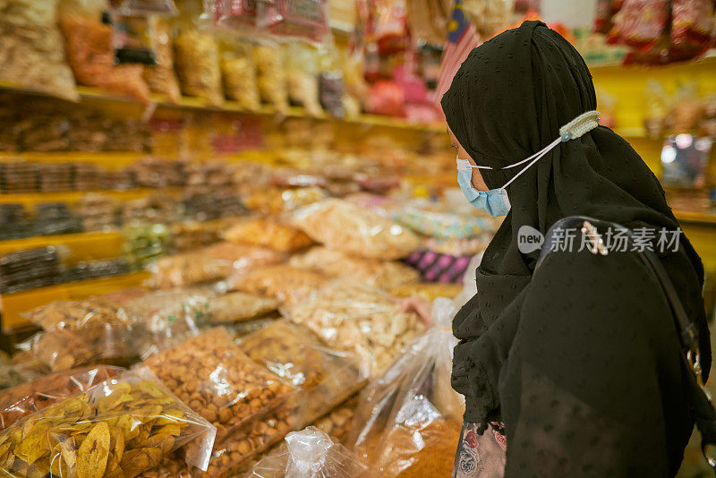 一名马来西亚妇女戴着头巾在小吃店购买包装好的食品
