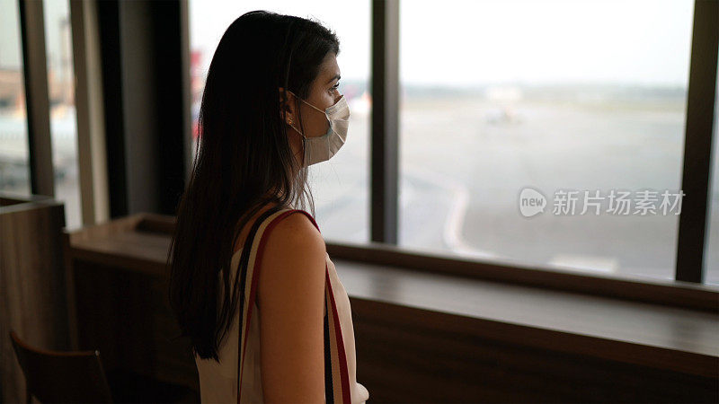 年轻的女旅客透过窗户看机场，戴着口罩