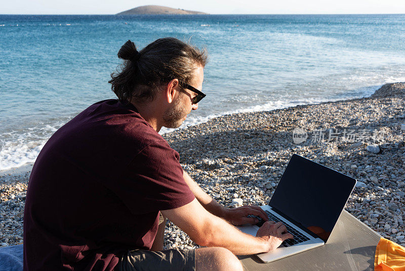 年轻的商人在海边用笔记本电脑工作